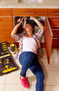Jeune femme en train de réparer sa plomberie sous l'évier de la cuisine