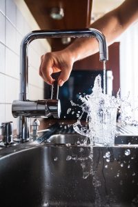 Personne en train d'activer un robinet de cuisine pour se servir une verre d'eau